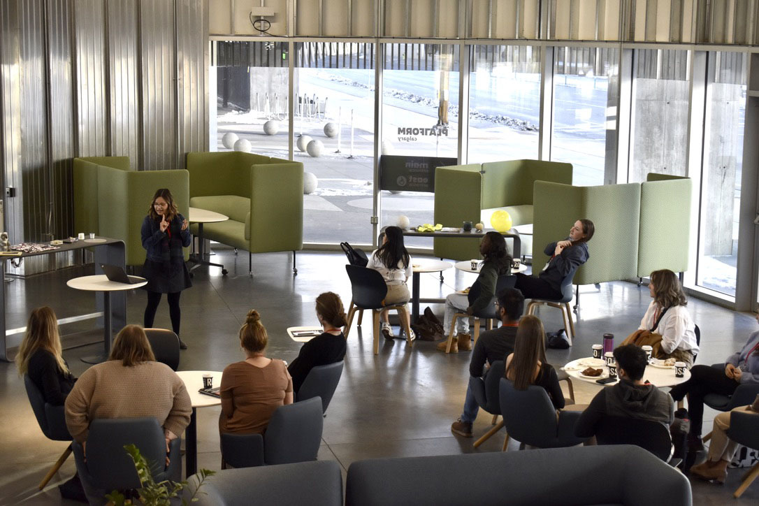 Many interns gather around a speaker in a bright windowed room